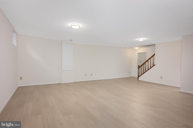 finished below grade area featuring stairway, light wood-style floors, and baseboards