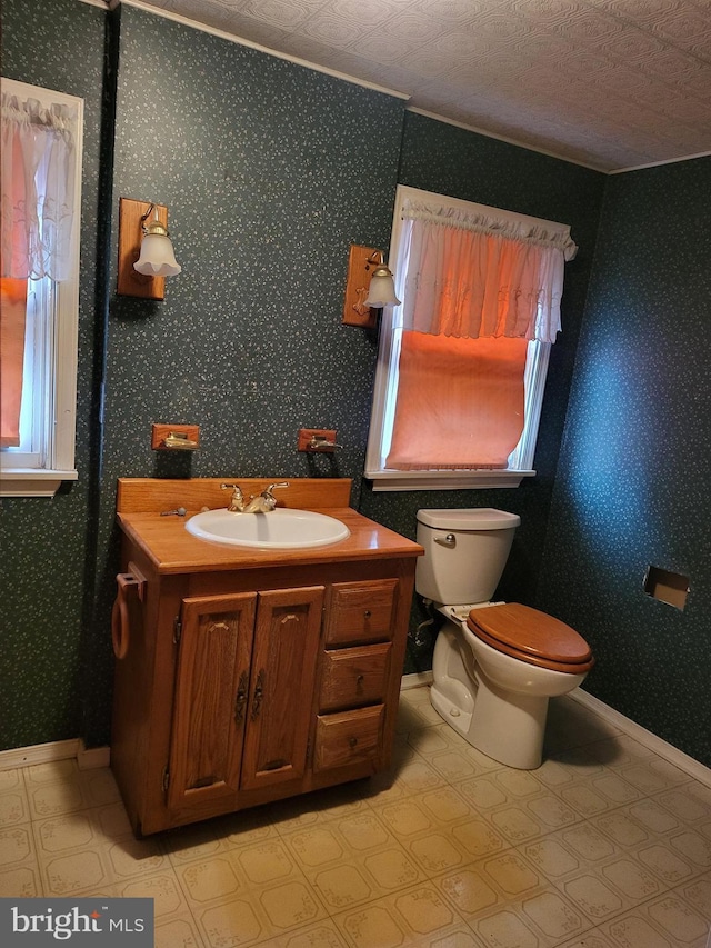 half bath featuring toilet, wallpapered walls, baseboards, and vanity