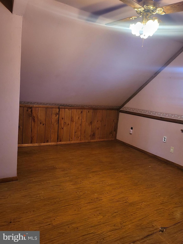 bonus room featuring wood walls, ceiling fan, vaulted ceiling, and dark wood-style flooring