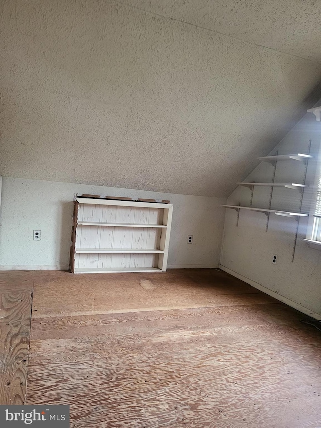 additional living space featuring vaulted ceiling, a textured ceiling, and wood finished floors