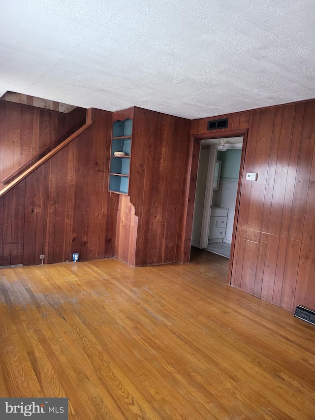 spare room with a textured ceiling, light wood finished floors, wood walls, and visible vents