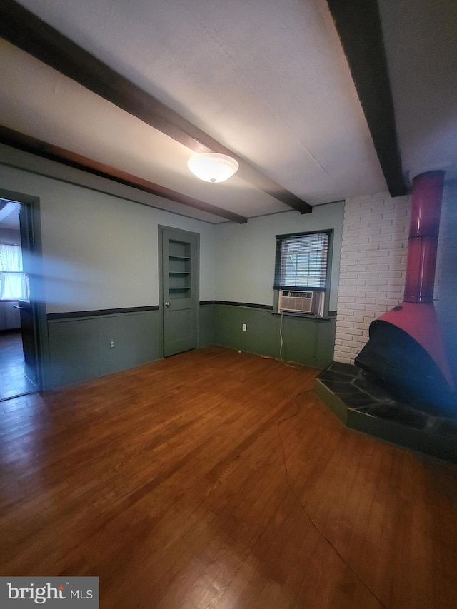 unfurnished living room featuring wainscoting, cooling unit, beamed ceiling, and wood finished floors