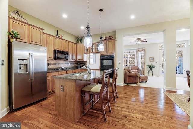 kitchen with light wood-style floors, a breakfast bar, backsplash, black appliances, and a sink