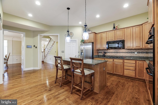 kitchen with stainless steel fridge, a kitchen island, a breakfast bar, black microwave, and gas cooktop