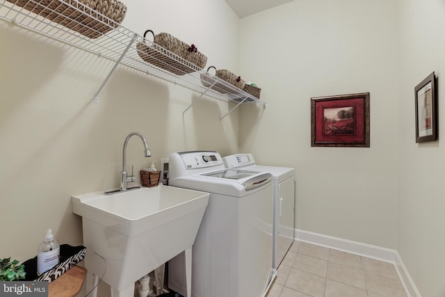 washroom featuring light tile patterned floors, laundry area, a sink, baseboards, and washing machine and clothes dryer