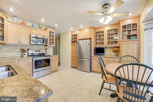 kitchen featuring light tile patterned floors, glass insert cabinets, light brown cabinets, and appliances with stainless steel finishes