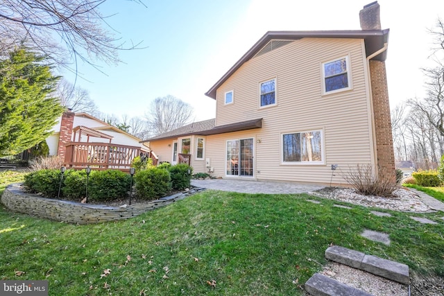 rear view of house featuring a deck, a lawn, a chimney, and a patio