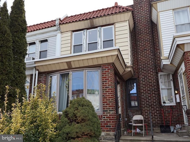 townhome / multi-family property with brick siding, a patio area, and a tile roof