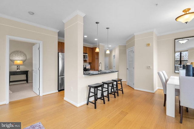 kitchen featuring appliances with stainless steel finishes, a breakfast bar, brown cabinets, and ornamental molding