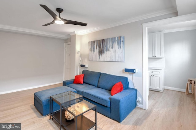 living room with ornamental molding, light wood-style flooring, baseboards, and a ceiling fan