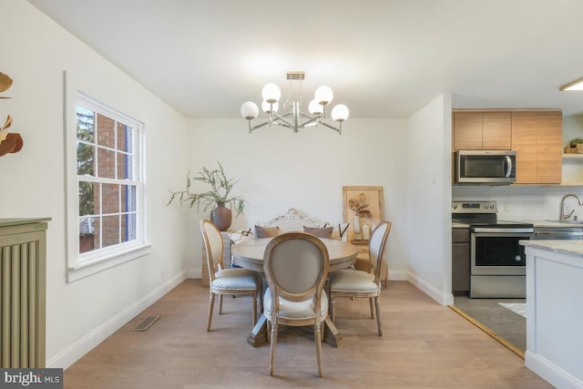 dining space featuring light wood-style floors, baseboards, visible vents, and a notable chandelier