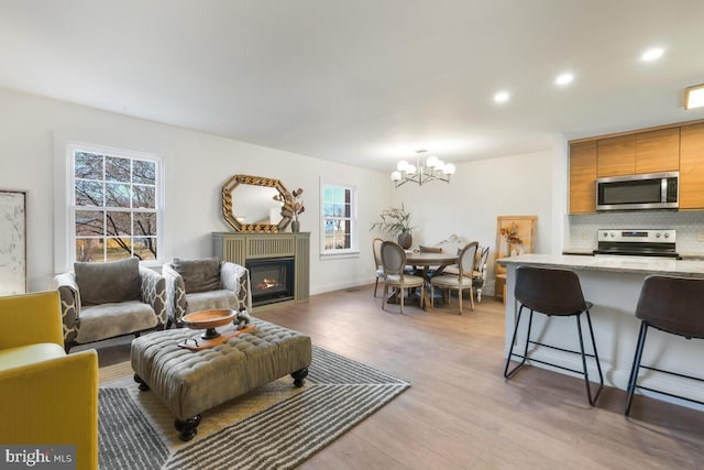 living room with light wood finished floors, a glass covered fireplace, a wealth of natural light, and recessed lighting