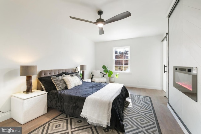 bedroom with ceiling fan, a barn door, wood finished floors, and baseboards