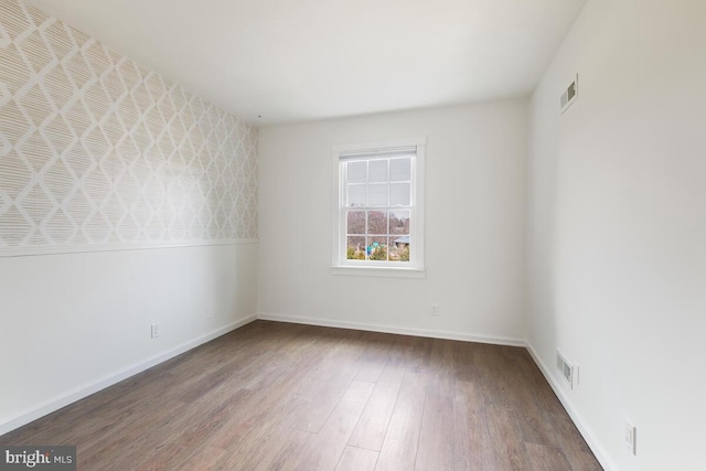 unfurnished room featuring baseboards, visible vents, and wood finished floors