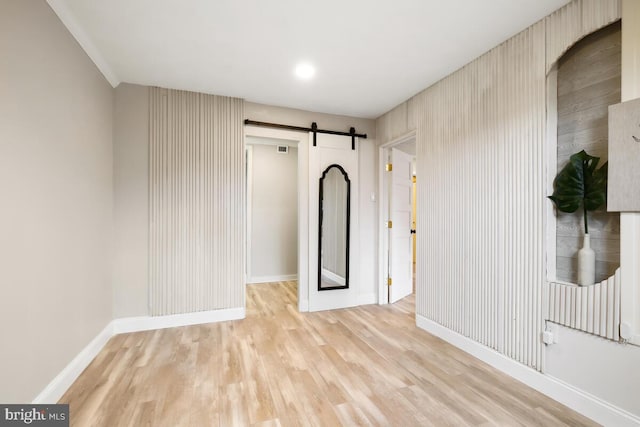 unfurnished room featuring light wood-type flooring, a barn door, visible vents, and baseboards