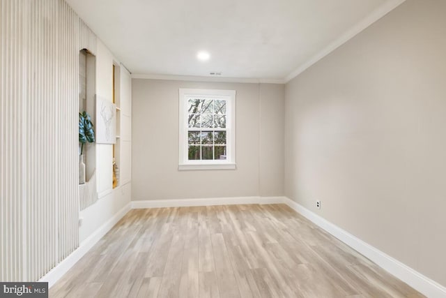 spare room featuring light wood finished floors, visible vents, baseboards, and crown molding