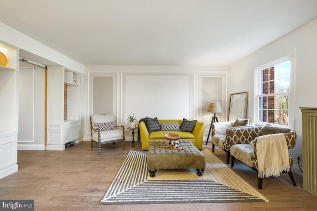 living area featuring light wood-style flooring, built in shelves, and a decorative wall