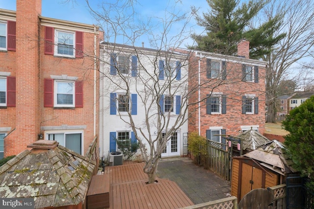 back of property featuring brick siding, a chimney, a wooden deck, and central AC unit