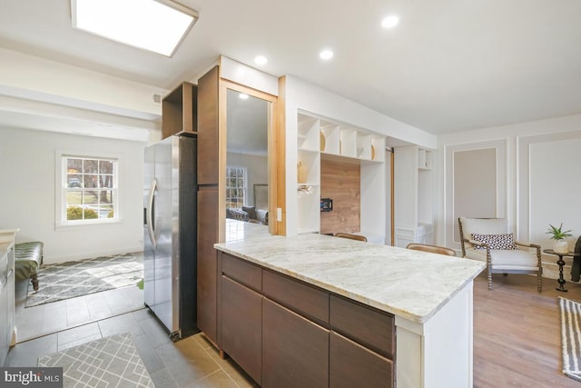 kitchen with recessed lighting, stainless steel refrigerator with ice dispenser, dark brown cabinets, and light stone countertops