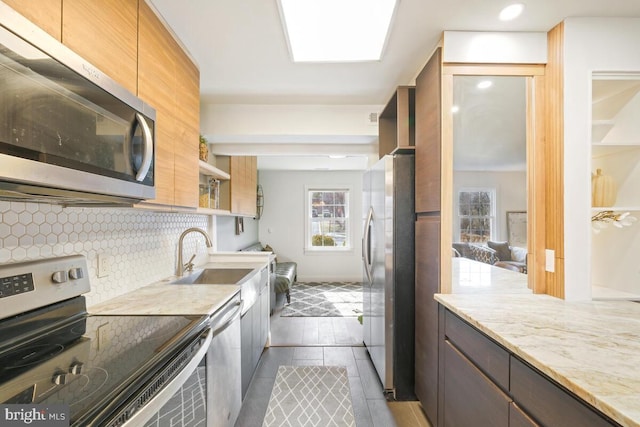 kitchen featuring appliances with stainless steel finishes, a sink, light stone countertops, open shelves, and backsplash