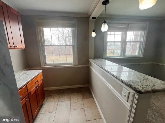 kitchen featuring light stone counters, a peninsula, baseboards, hanging light fixtures, and crown molding