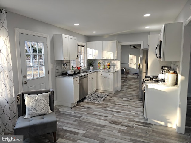 kitchen with stainless steel appliances, a healthy amount of sunlight, light stone countertops, and white cabinets
