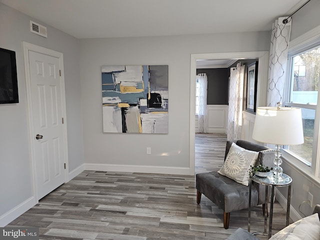 living area featuring baseboards, visible vents, wood finished floors, and wainscoting