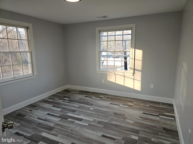 spare room with dark wood-type flooring, visible vents, and baseboards