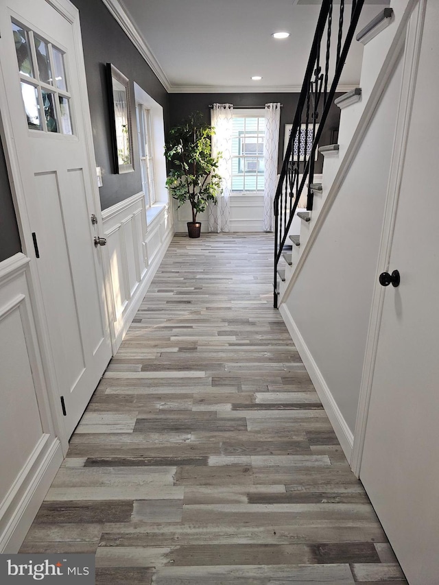 entrance foyer with crown molding, recessed lighting, a decorative wall, stairway, and light wood-style flooring