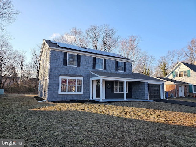 view of front of house featuring covered porch, a garage, driveway, roof mounted solar panels, and a front yard