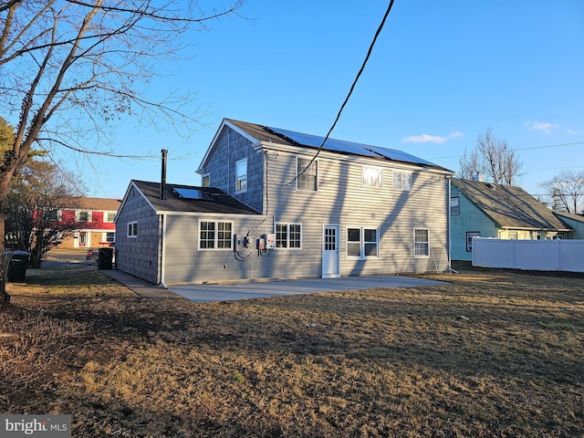 back of property featuring a yard, roof mounted solar panels, a patio area, and fence