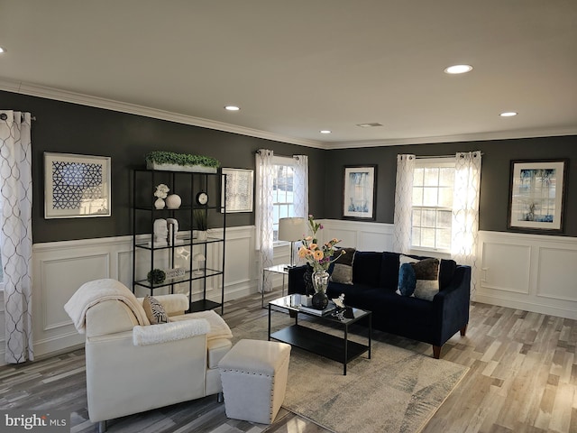 living area with a wainscoted wall, ornamental molding, and light wood-style floors