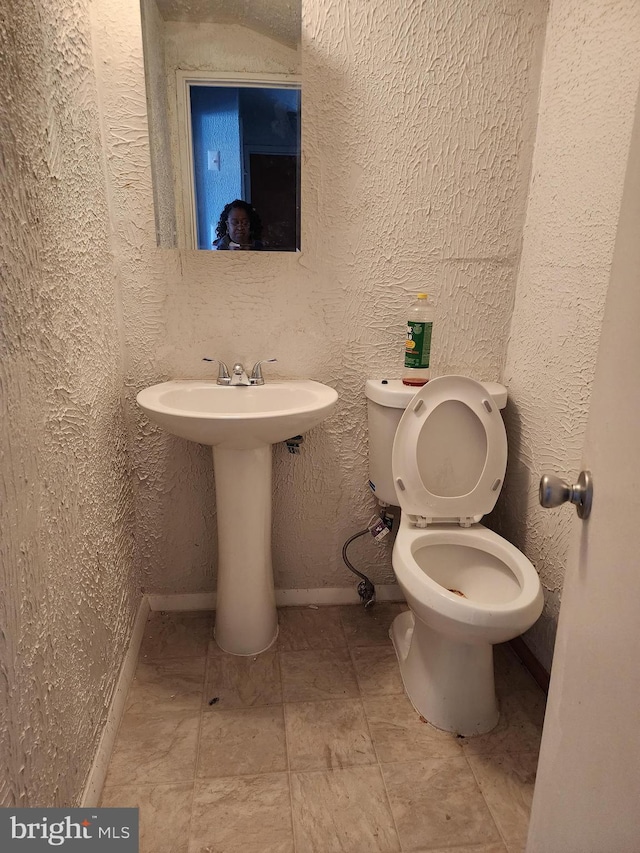 bathroom with toilet, baseboards, and a textured wall