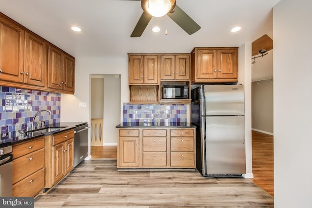 kitchen featuring brown cabinetry, dark countertops, light wood-style flooring, stainless steel appliances, and a sink