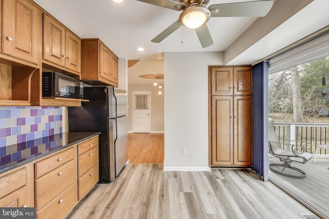 kitchen with black microwave, light wood-style flooring, freestanding refrigerator, tasteful backsplash, and dark stone countertops