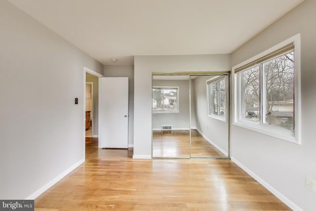 unfurnished bedroom featuring visible vents, a closet, light wood-style flooring, and baseboards