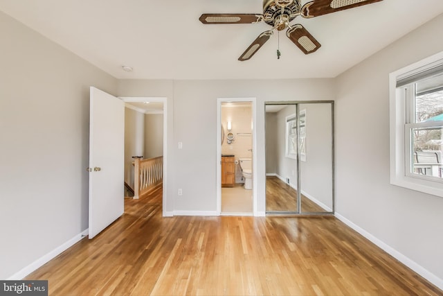 unfurnished bedroom with a closet, connected bathroom, baseboards, and wood finished floors