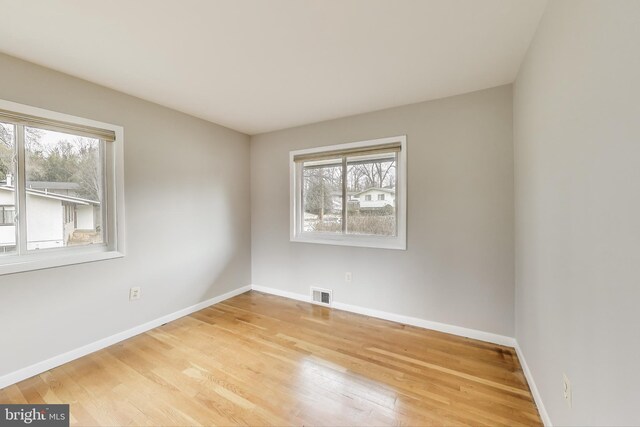 spare room featuring light wood-type flooring, visible vents, and baseboards