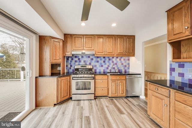 kitchen with appliances with stainless steel finishes, brown cabinets, dark stone countertops, under cabinet range hood, and a sink