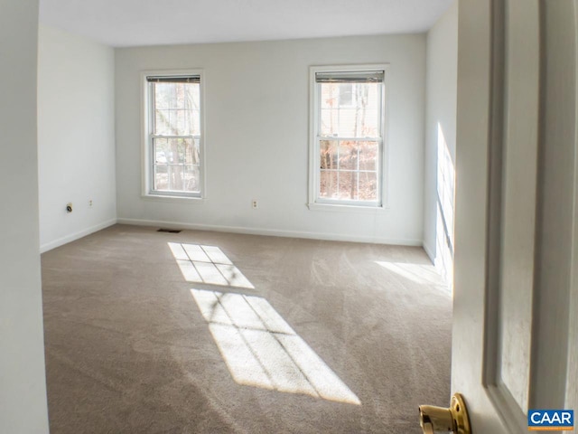 carpeted empty room featuring a wealth of natural light, visible vents, and baseboards