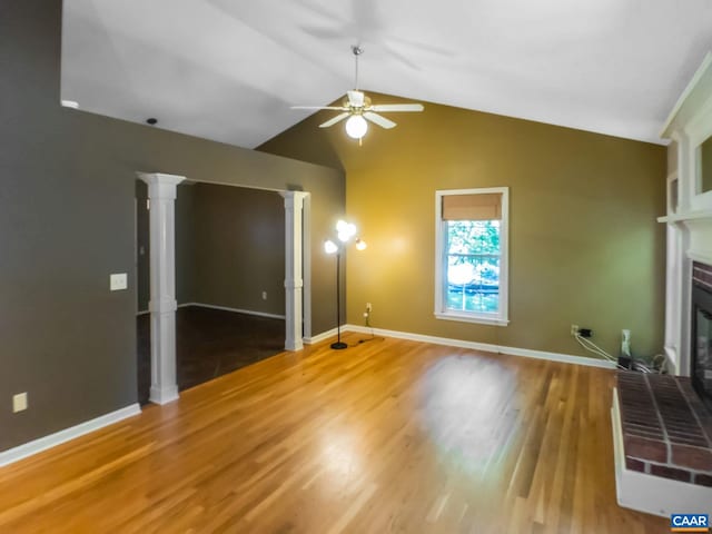 unfurnished living room featuring vaulted ceiling, a brick fireplace, wood finished floors, and baseboards