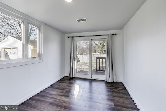 empty room featuring dark wood-type flooring, visible vents, and baseboards