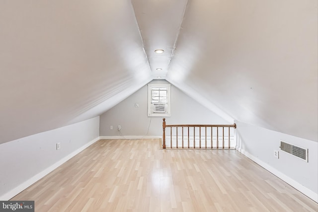 additional living space with vaulted ceiling, wood finished floors, visible vents, and baseboards