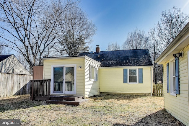 rear view of house with a chimney, fence, and roof with shingles