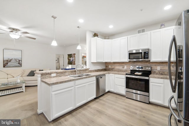 kitchen featuring appliances with stainless steel finishes, open floor plan, hanging light fixtures, a peninsula, and a sink