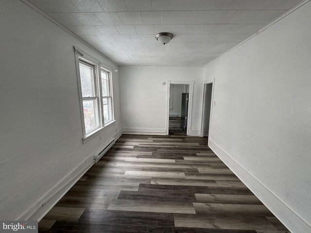 empty room featuring dark wood-style floors, crown molding, baseboard heating, and baseboards