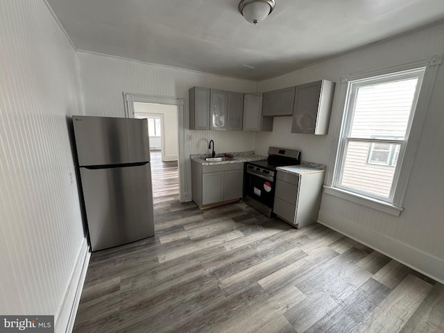 kitchen featuring a sink, a healthy amount of sunlight, appliances with stainless steel finishes, gray cabinets, and light wood finished floors