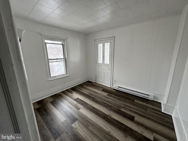 empty room featuring a baseboard radiator, baseboards, and dark wood-type flooring