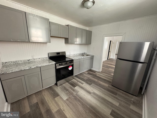 kitchen featuring dark wood-style flooring, gray cabinetry, appliances with stainless steel finishes, a sink, and light stone countertops