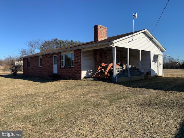 rear view of property featuring brick siding, a lawn, and a chimney